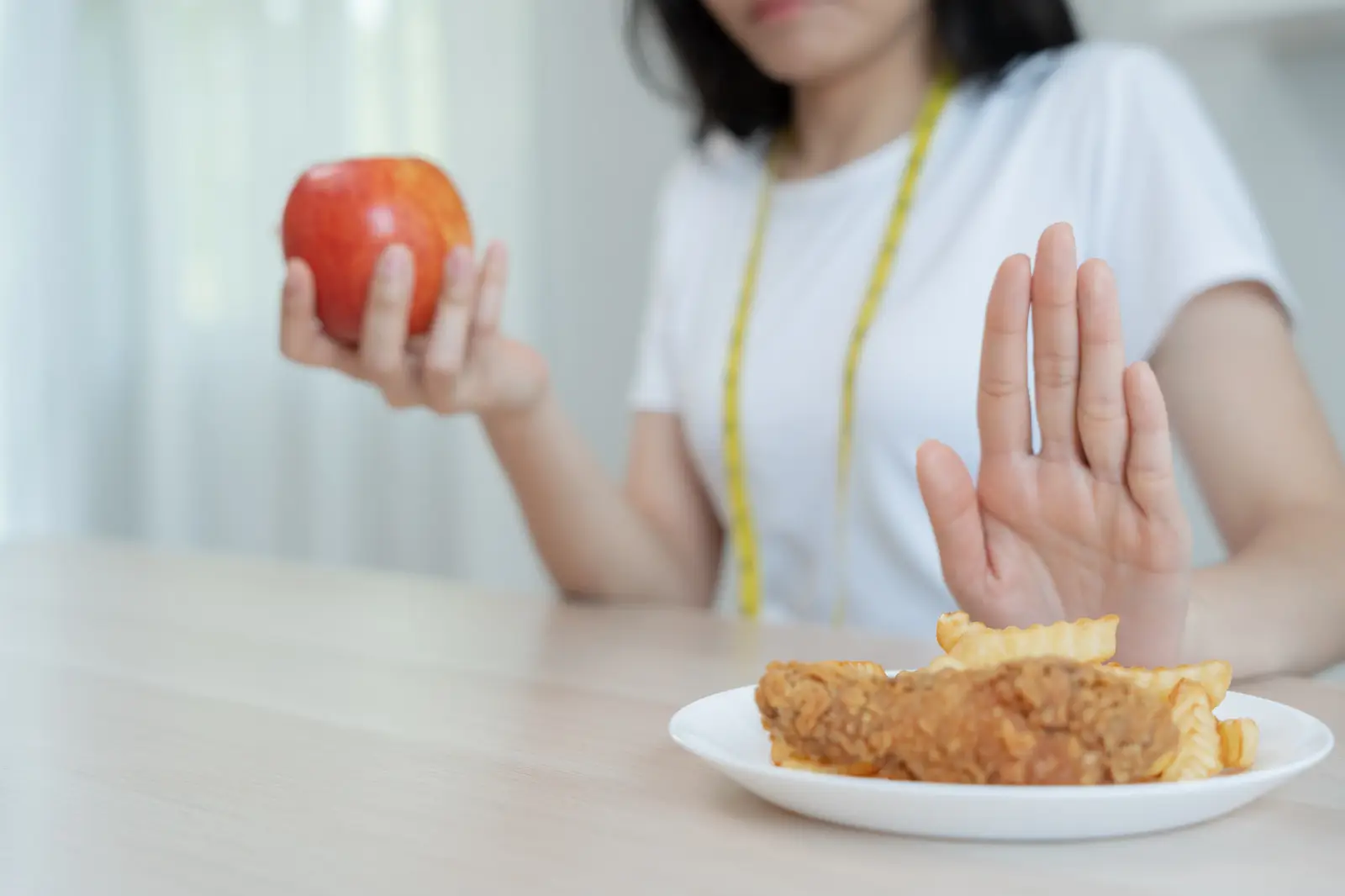Femme tenant une pomme et refusant un plat frit, illustrant le choix d’une alimentation saine pour brûler les graisses et perdre du poids.