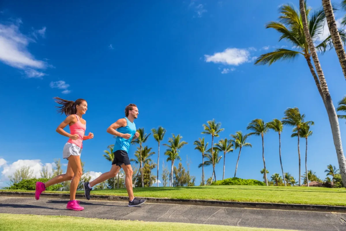 Homme et femme courant en extérieur sous un ciel ensoleillé, illustrant l'importance du cardio pour la perte de poids et le bien-être.