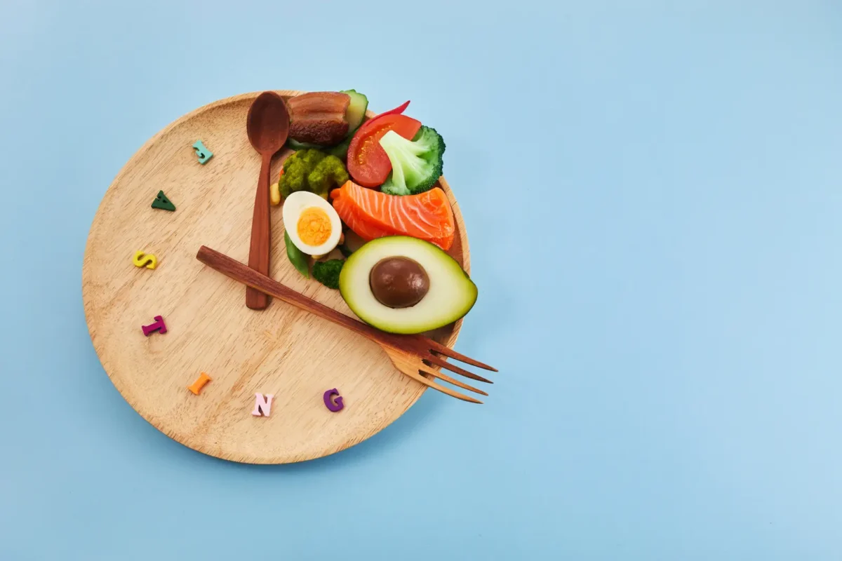 Assiette en bois illustrant le jeûne intermittent avec une portion de nourriture saine et des couverts disposés comme une horloge.